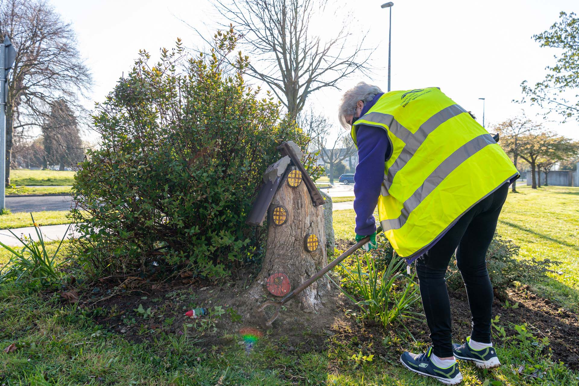 Volunteer tending a planted area beside a decorative tree stump feature during a community event