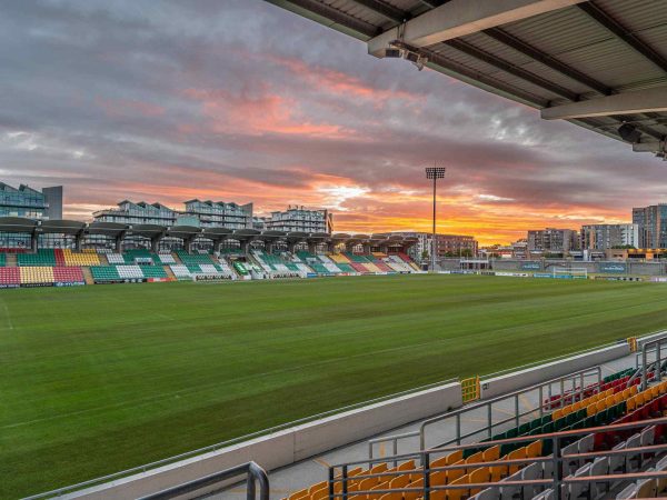 Wide view of Tallaght Stadium in Tallaght, with empty seating and football pitch under a dramatic sunset sky